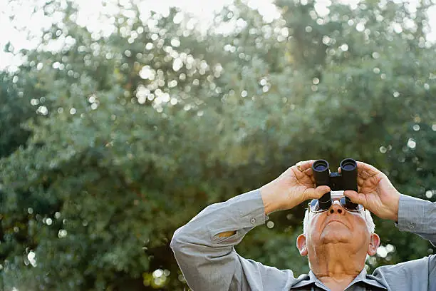 At the bottom right of the frame, an older man in a grey top is looking through binoculars, pointed upwards