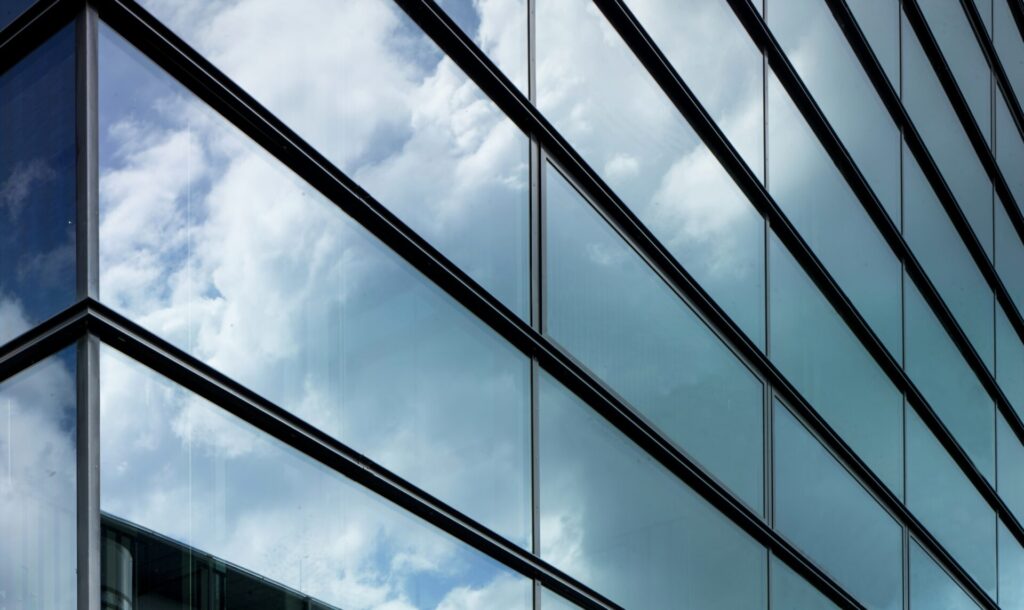 Photo showing the glass windows of a high-rise building reflecting the sky and clouds. 